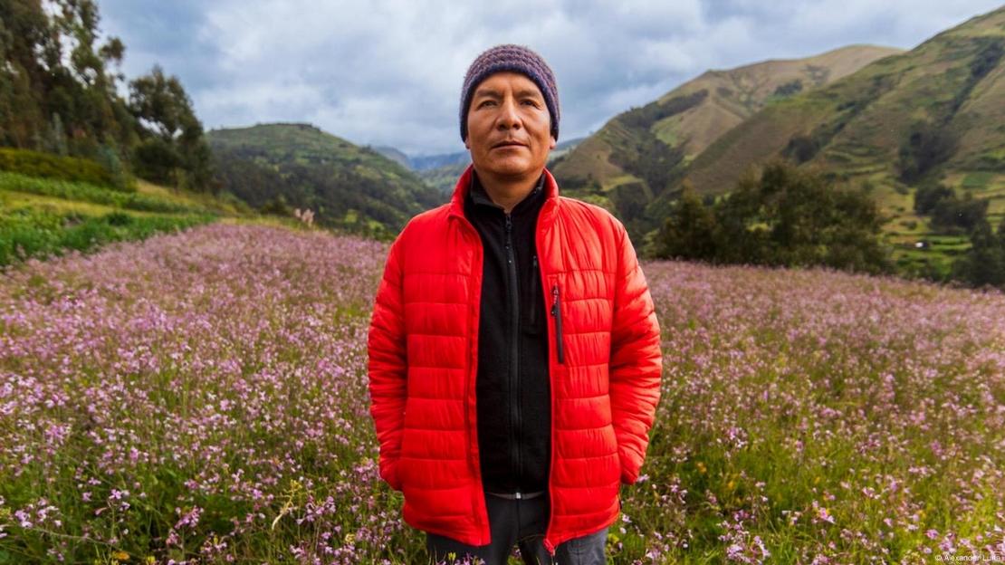 Ativista peruano do clima Saúl Luciano Lliuya em uma paisagem florida, com montanhas ao fundo