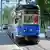 A blue tram on a street, a car running alongside it