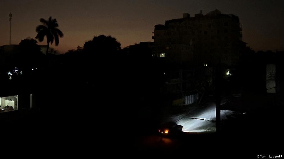 Fotografía de alta calidad de Cuba durante un apagón, con un enfoque en la oscuridad que envuelve las ciudades y la gente usando linternas, capturando el impacto del corte de energía. Estilo documental y realista.