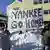 Demonstranten mit einem Banner "Yankee go home"