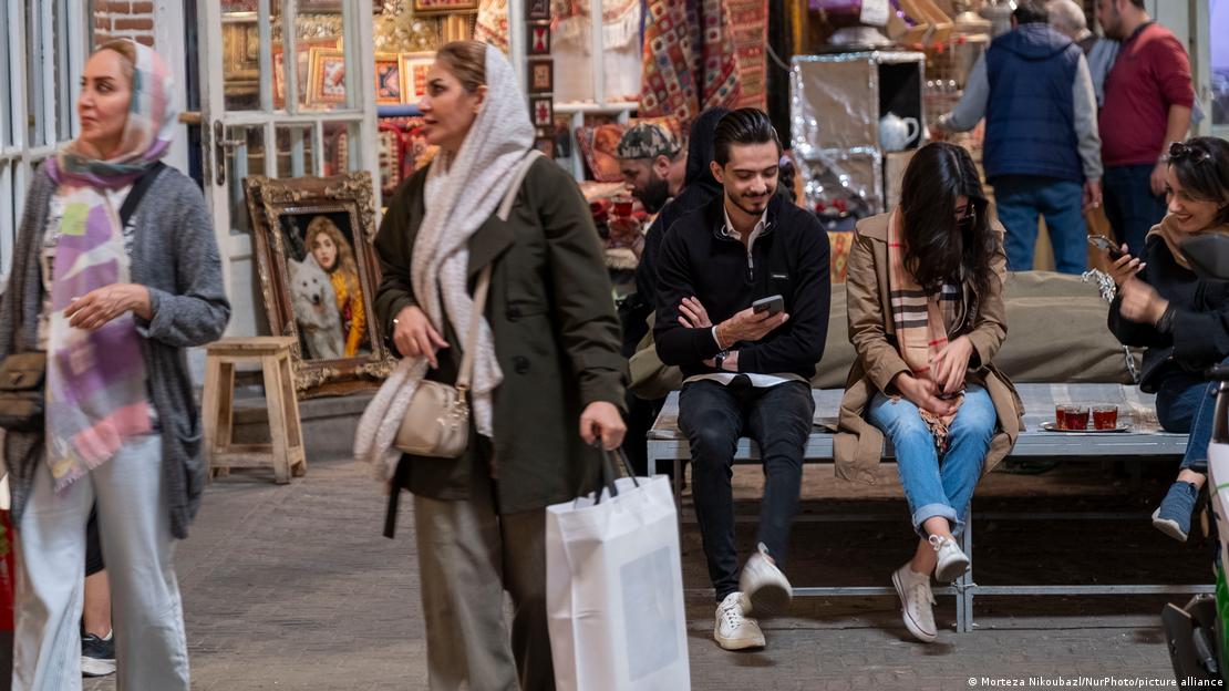 ایرانی شہر تبریز کے گرینڈ بازار سے شاپنگ کر کے گزرتی دو خواتین اور پس منظر میں بیٹھے ہوئے چند نوجوان ایرانی شہر تبریز کے گرینڈ بازار سے شاپنگ کر کے گزرتی دو خواتین اور پس منظر میں بیٹھے ہوئے چند نوجوان