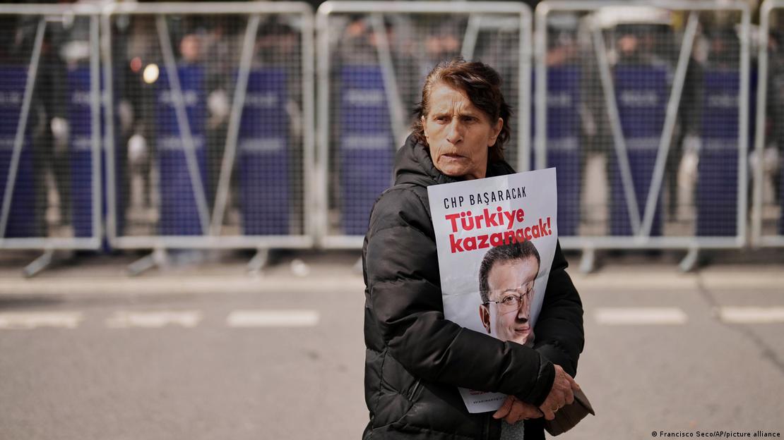 Elinde İmamoğlu'nun posteri bulunan bir kadın, arka planda kalkanları ile polisler var