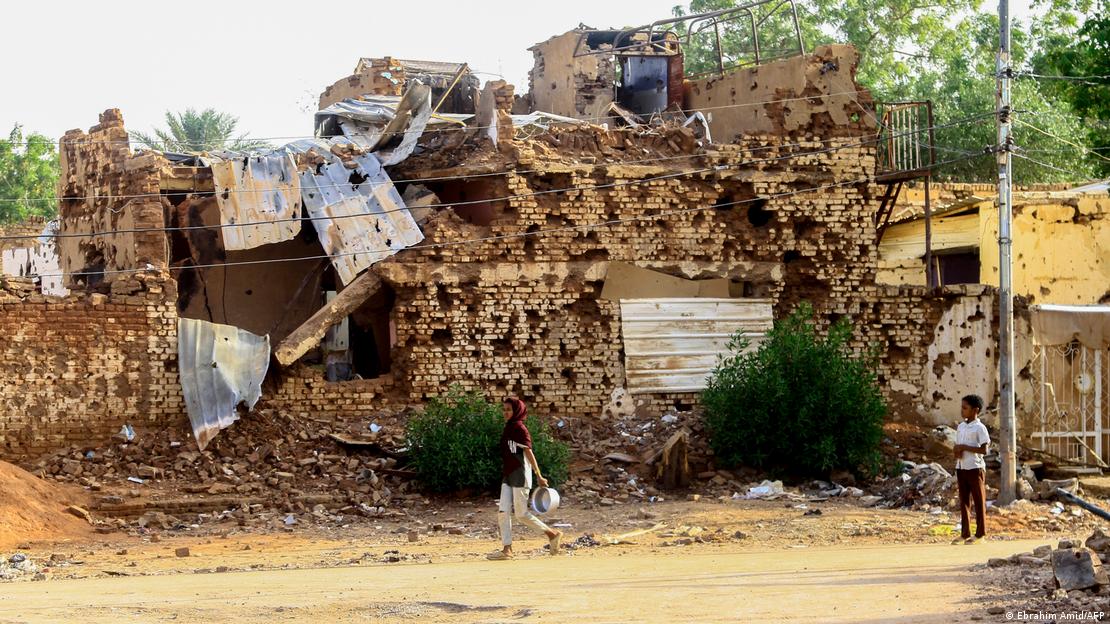 Un niño sudanés observa mientras una mujer pasa junto a un edificio dañado en Omdurman, la ciudad gemela de Jartum, el 20 de marzo de 2025.