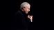 András Schiff von der Seite mit gefalteten Händen vor schwarzem Hintergrund András Schiff von der Seite mit gefalteten Händen vor schwarzem Hintergrund