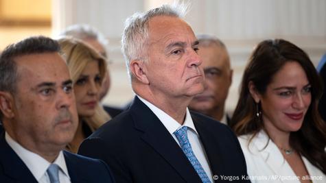 Двајца мажи во темни одела и една жена во бело палто. Во средината е грчкиот министер за миграција Макис Воридис Двајца мажи во темни одела и една жена во бело палто. Во средината е грчкиот министер за миграција Макис Воридис