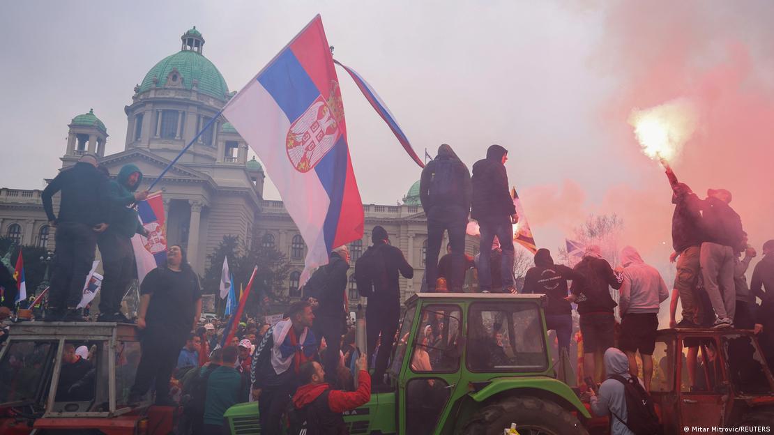 Demonstrierende stehen auf Traktoren, rechts im Bild schwenkt jemand eine Fackel, links im Bild ein junger Mann mit einer serbischen Fahne Demonstrierende stehen auf Traktoren, rechts im Bild schwenkt jemand eine Fackel, links im Bild ein junger Mann mit einer serbischen Fahne