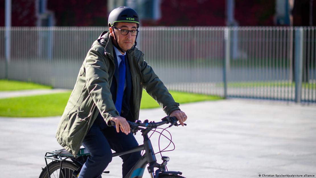 Eski Tarım Bakanı Cem Özdemir, bisikleti üzerinde kameralara bakıyor. Özdemir'in başında kaskı bulunuyor.