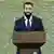 Syria's interim President Ahmed al-Sharaa, wearing a suit and tie, stands at a podium to announce the formation of a new government late on March 29, 2025.