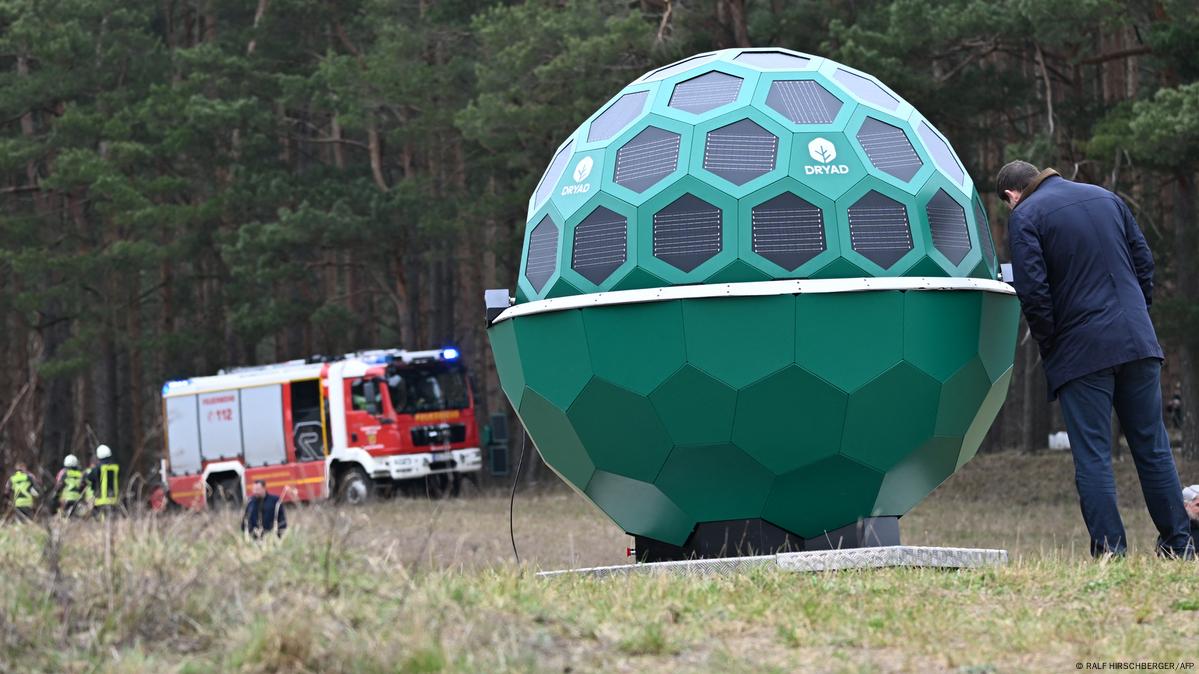 Një sistem droni i bazuar në inteligjencën artificiale nga kompania e teknologjisë së sensorëve Dryad. Duket si një top i madh jeshil dhe qëndron përpara një pylli, me një kamion zjarrfikës të dukshëm në sfond.