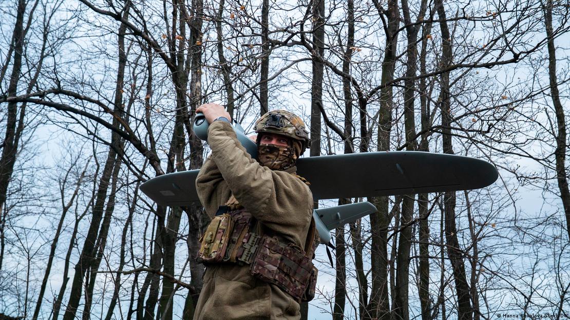 Soldado ucraniano carrega drone nas costas, em meio a bosque.