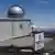 The Mauna Loa Observatory. Clouds and the sea are in the background of the research station and a sign announcing the observatory is in the foreground