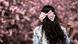 A woman with dark hair wearing a pink bow in her hair seen from behind. A pink blooming cherry tree is in the background out of focus A woman with dark hair wearing a pink bow in her hair seen from behind. A pink blooming cherry tree is in the background out of focus