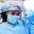 A woman wears personal protective medical clothing, such as latex gloves, a hair net and face mask.