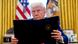 Donald Trump holds an executive order booklet in the Oval Office, with the American flag and Presidential standard in the background. Donald Trump holds an executive order booklet in the Oval Office, with the American flag and Presidential standard in the background.