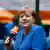 Deutschlands frühere Bundeskanzlerin Angela Merkel in einer blauen Jacke, sie hält ein orangenes Mikrophon in der Hand