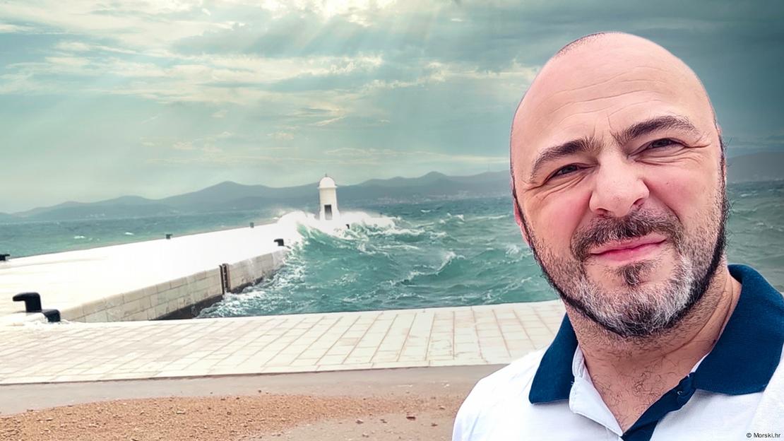 Ćelavi muškarac s bradom stoji na obali ispred uzburkanog mora Ćelavi muškarac s bradom stoji na obali ispred uzburkanog mora