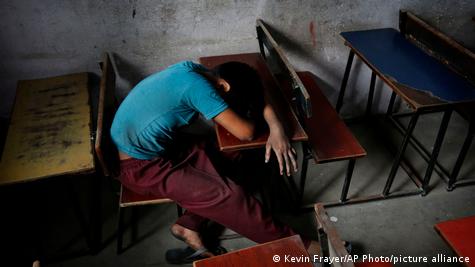 Un niño descansa sobre un pupitre escolar luego de trabajar, en India.