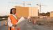 Mujer con chaleco reflectante y casco con plano en sus manos frente a una construcción. Mujer con chaleco reflectante y casco con plano en sus manos frente a una construcción.