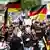Manifestación de extrema derecha en Berlín: jóvenes con banderas alemanas y, en el centro, un joven con una camiseta en la que se lee la palabra "Heimat", que se traduce como "patria" y es el nuevo nombre del partido neonazi antes denominado NPD.