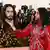 Picture of a bearded, long-haired man dressed in red holding up a replica of his head.