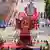A large float in the shape of a a pink lotus blossom holds the potrait of Ho Chi Minh. Soldiers line the street waving Vietnamese flags.
