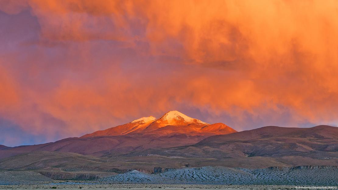 Colorida imagen del volcán Uturuncu, con la cima nevada y un cielo naranja al fondo.