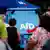 Pessoas de costas olhando para cartaz com logo da AfD