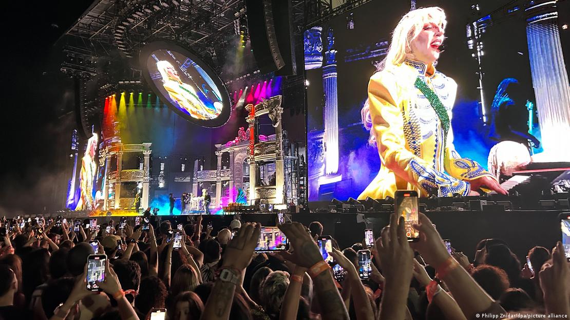 Lady Gaga auf einer Großleinwand - davor zahllose erhobene Arme ihrer Fans 