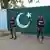 Pakistan'da füzeyle vurulan bir bölge yakınlarındaki güvenlik güçleri ve arkalarında Pakistan bayrağı motifli kapı