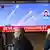 People sit and stand around a large TV screen in South Korea on May 8, 2025, showing missiles fired by North Korea flying across a clear blue sky.
