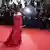 A woman in an elegant dress with her back to the camera stands on the red carpet while being photographed by tons of photographers