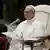 Papst Leo XIV. sitzt in einem weißen Sitz vor einem Mikrofon
