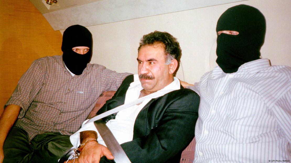 1999 yılında Kenya'da yakalanan PKK lideri Abdullah Öcalan'ın uçakla Türkiye'ye getirilirken maskeli Türk güvenlik güçleri eşliğinde elleri bağlı olarak çekilmiş fotoğrafı 1999 yılında Kenya'da yakalanan PKK lideri Abdullah Öcalan'ın uçakla Türkiye'ye getirilirken maskeli Türk güvenlik güçleri eşliğinde elleri bağlı olarak çekilmiş fotoğrafı