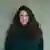 A woman with long, dark wavy hair smiles at the camera.