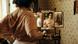 A film still from 'Sound of Falling': A woman dresses while she looks into a mirror showing different parts of her body, the room features period wallpaper. A film still from 'Sound of Falling': A woman dresses while she looks into a mirror showing different parts of her body, the room features period wallpaper.