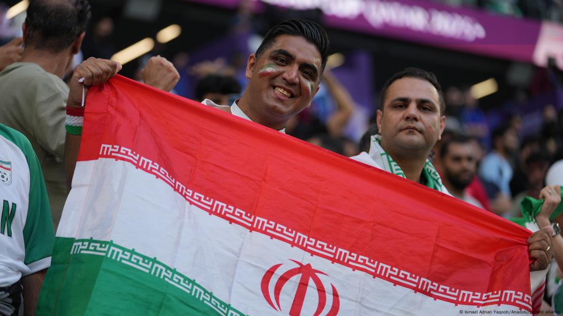 Dos iranies apoyando su seleccion nacional en las tribunas sosteniendo su bandera.