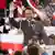 A man (Rafal Trzaskowski) stands at a microphone, smiling and waving to his supporters. Behind him, people wave the red-and-white flag of Poland, Krakow, Poland, May 13, 2025
