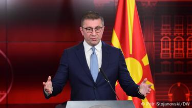 Македонскиот премиер Христијан Мицкоски држи прес-конференција облечен во темно син костум, бела кошула и светло сина вратоврска. Зад него е македонското знаме Македонскиот премиер Христијан Мицкоски држи прес-конференција облечен во темно син костум, бела кошула и светло сина вратоврска. Зад него е македонското знаме