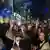 Men and women, some making a victory sign with their fingers and some waving EU and Romanian flags, celebrate on a street at night after polls closed for the second round of the country's presidential election, Bucharest, Romania, Sunday, May 18, 2025
