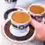 Una mano lleva dos tazas chicas de café.