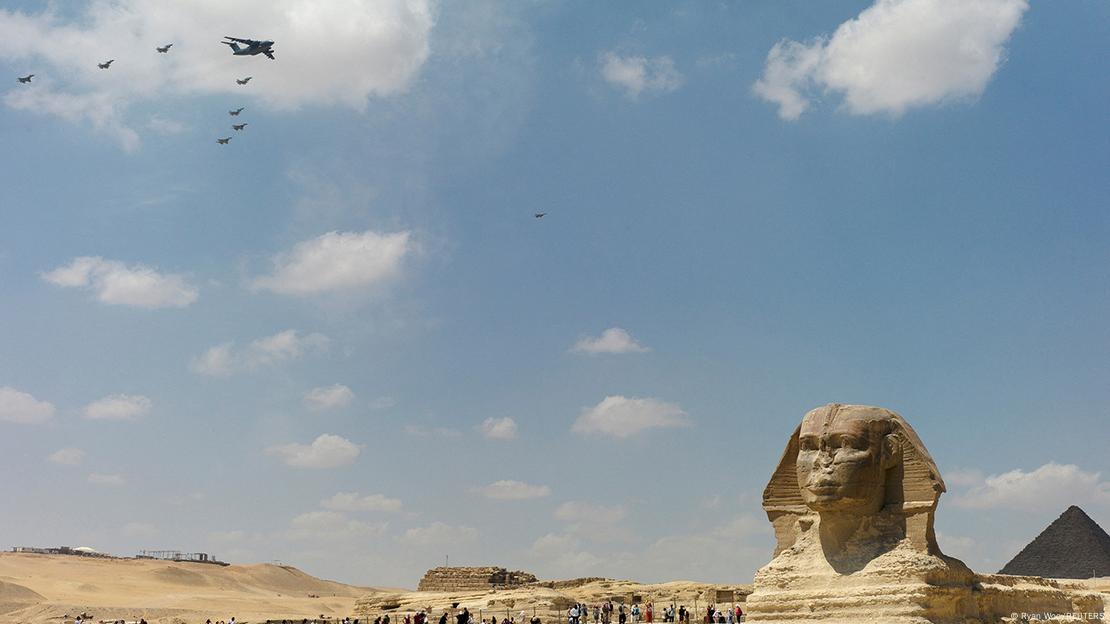 Military aircraft fly in formation, as tourists look on, at the Giza pyramid complex