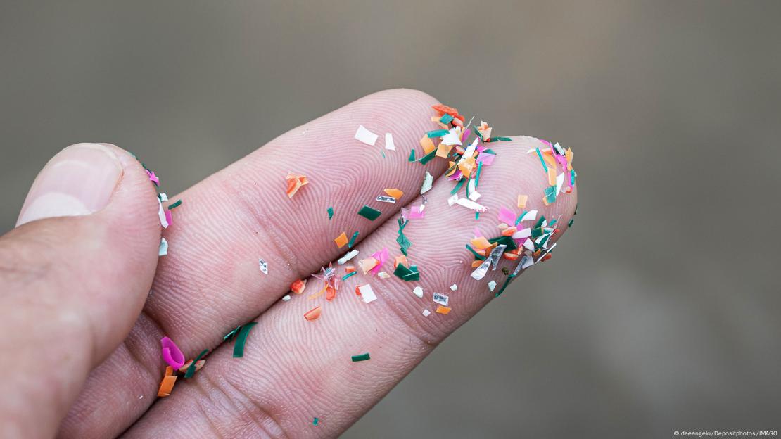 Una mano con microplásticos pegados a los dedos.