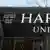 Se ve parte del escudo y la inscripción "Harvard University" en la puerta de uno de los edificios de la universidad, con el edificio de enfrente reflejado en el cristal.