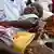 A child is being held up in the arms of her mother, while a healthcare worker's hand is seen administering an injection