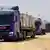 Large blue trucks carrying aid drive along dirt roads