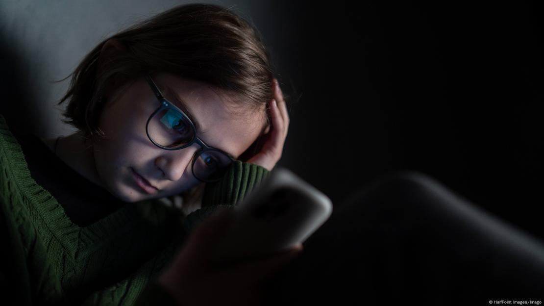 Una joven con un teléfono móvil en un lugar oscuro. Una joven con un teléfono móvil en un lugar oscuro.