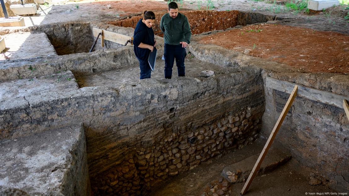 Arqueólogos observan la antigua casa y sitio de excavación donde fue hallado el trozo de pan.