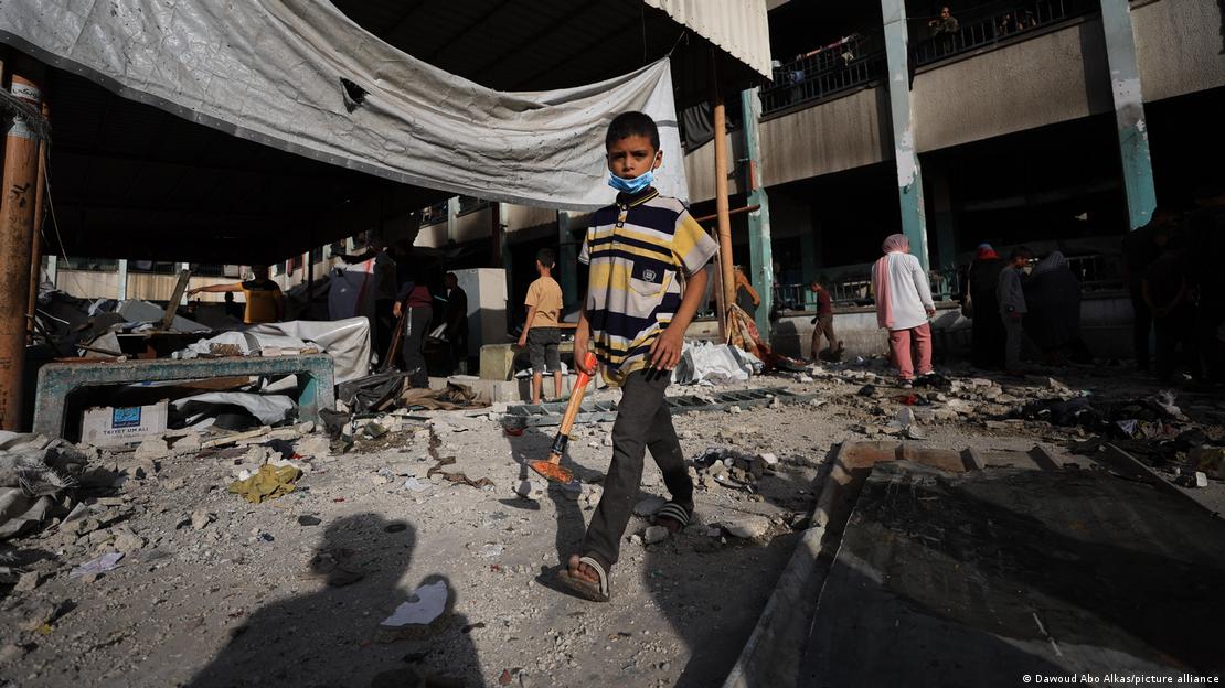 Gazze'de İsrail saldırılarından kaçarak Fehmi El Cercavi okulunu sığınan Filistinli bir erkek çocuğu enkaz üzerinde yürüyor