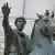 A close-up of a bronze equestrian statue showing a bearded, curly-headed man on a horse, raising his right hand. The horse wears a Roman-style bridle.