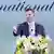 Eric Trump points with his hand while speaking in front of some flowers on a stage